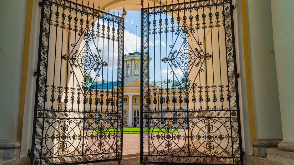 Elegant wrought iron gates open to reveal a neoclassical palace on a clear day.